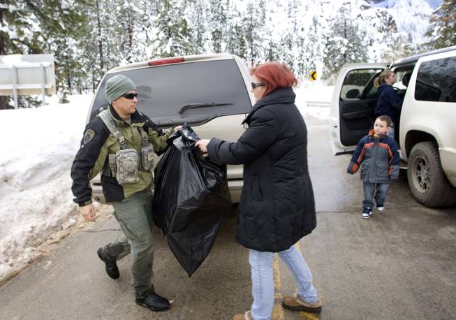 Metro Police search and rescue officer David Vanbuskirk hands a bag of Christmas presents to Kim Koster at the entrance to the Echo subdivision of Kyle Canyon on Thursday, Dec. 23, 2010. Koster said she left her cabin to get gas for the generator, then came back to find out about the avalanche warning. Search and rescue officers went to her home and picked up her dog and Christmas presents. Areas of Kyle Canyon received between 37 and 90 inches of snow from the recent storm.
