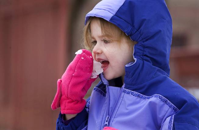 Kathleen McCarthy, 3, takes a bite of snow while building a snowman with her father in a Summerlin park Monday, January 3, 2011.  