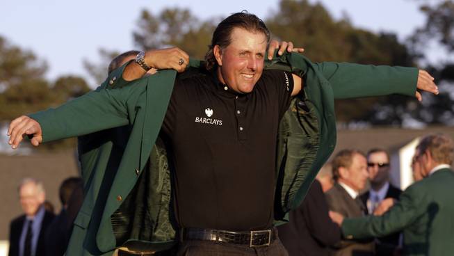 Phil Mickelson slips into his green jacket after winning his third Masters championship last year at Augusta National in Augusta, Ga.