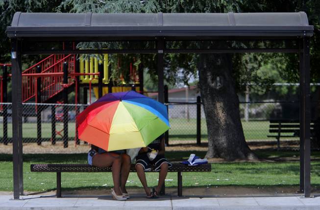 A couple of public transit riders take shelter from the heat under an umbrella at a bus stop Thursday, May 18, 2006, in Fresno, Calif.