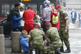 Wounded people are treated in the street in the centre of Oslo, Norway, Friday, July 22, 2011, following an explosion that tore open several buildings including the prime minister's office, shattering windows and covering the street with documents and debris.