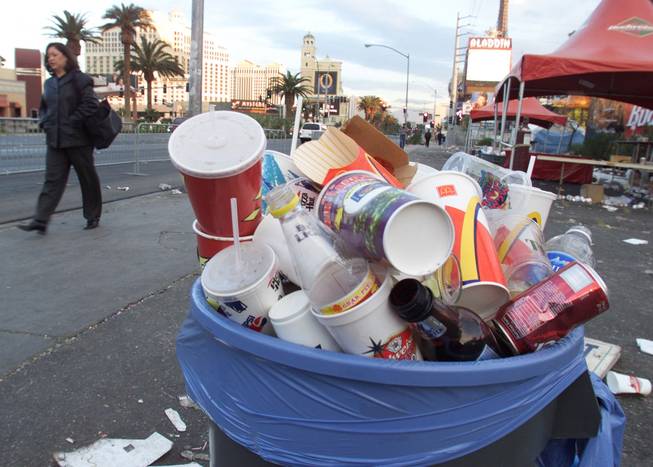 A pedestrian walks past a can full of garbage on the Strip.