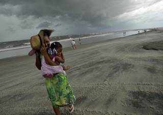 Kia Head carries Christian Searcy in her arms while protecting their faces from wind and sand blown in from Hurricane Irene in Tybee Island, Ga., Friday, Aug. 26, 2011. 
