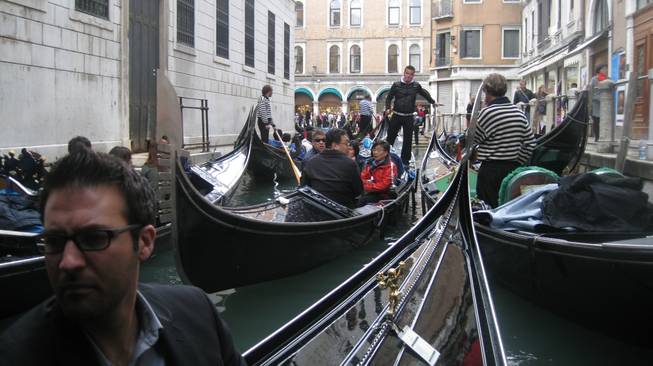 A gondola is navigated through a busy canal in Venice. The guy in the foreground is Tony Moreno.