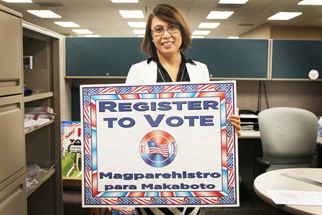 May Manahan, elections operations specialist for Clark County, holds a sign that reads "register to vote" in English and Filipino. In October the federal government informed the county that, based on demographic data, elections materials must be translated into Filipino.
