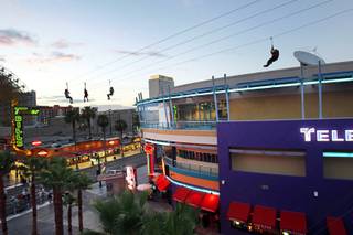 People travel down zip lines in front of the Neonopolis mall in downtown Las Vegas Wednesday, August 1, 2012.