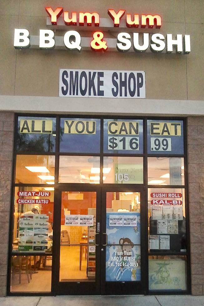 The store front of the Yum Yum BBQ & Sushi restaurant advertises their all you can eat sushi and smoke shop cigarette brands.