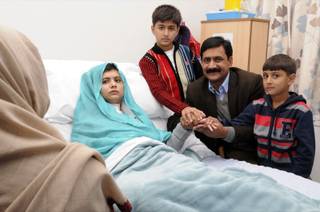 In this undated handout photo issued by Queen Elizabeth Hospital, in Birmingham, England, on Friday, Oct. 26, 2012, Malala Yousufzai in her hospital bed, poses for a photograph, with her father Ziauddin, second right accompanied by her two younger brothers Atal, right and Khushal, centre. 