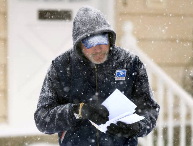 In this Saturday Dec. 19, 2009, file photo, U. S. Post Office letter carrier Tim Bell delivers the mail during a snow storm in Havertown, Pa.