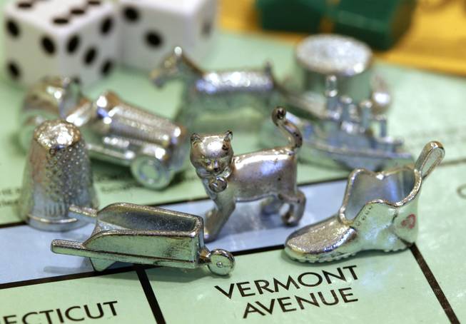 The newest Monopoly token, a cat, center, rests on a Boardwalk deed next to other tokens still in use including the wheelbarrow, left, and the shoe, right, at Hasbro Inc. headquarters, in Pawtucket, R.I., Tuesday, Feb. 5, 2013.  Voting on Facebook determined that the cat would replace the iron token.