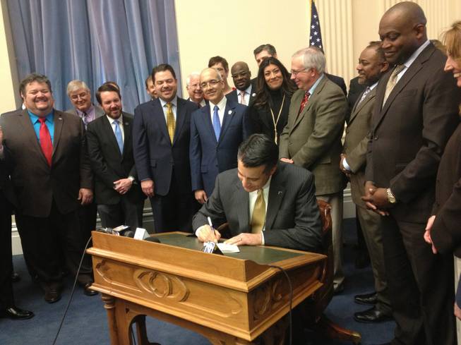 Surrounded by Nevada legislators, Gov. Brian Sandoval signs an online poker bill into law, Thursday, Feb. 21, 2013. The law will allow Nevada to move ahead with online poker in the absence of federal action.
