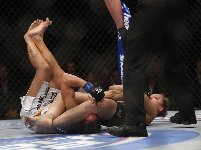 Liz Carmouche, left, taps out as Ronda Rousey pulls an armbar on her during their UFC 157 women's bantamweight championship mixed martial arts match in Anaheim, Calif., Saturday, Feb. 23, 2013. Rousey won the first womens bout in UFC history, forcing Carmouche to tap out in the first round. (AP Photo/Jae C. Hong)