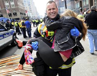 In this Monday, April 15, 2013 photo, Boston Firefighter James Plourde carries an injured girl away from the scene after a bombing near the finish line of the Boston Marathon in Boston. The FBI's investigation into the bombings at the Boston Marathon was in full swing Tuesday, with authorities serving a warrant on a suburban Boston home and appealing for any private video, audio and still images of the blasts that killed at least three and wounded more than 170. 