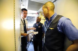 In this Thursday, May 9, 2013, photo, an Allegiant Air Capt. Bret Whalen, left, discusses the flight plan with flight attendants Antron Johnson, center, and John Taylor before their flight to Laredo, Tex, at McCarran International Airport in Las Vegas. While other U.S. airlines have struggled with the ups and downs of the economy and oil prices, tiny Allegiant Air has been profitable for 10 straight years.