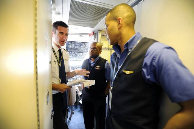 In this Thursday, May 9, 2013, photo, an Allegiant Air Capt. Bret Whalen, left, discusses the flight plan with flight attendants Antron Johnson, center, and John Taylor before their flight to Laredo, Tex, at McCarran International Airport in Las Vegas. While other U.S. airlines have struggled with the ups and downs of the economy and oil prices, tiny Allegiant Air has been profitable for 10 straight years.