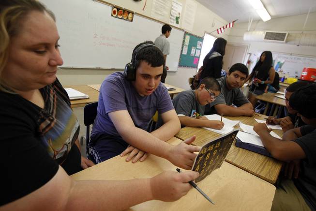 Ido Kedar, second from left, who is a non-verbal autistic teenager, answers a question with the use of a letter board held by behavior intervention implementer Anna Page during a class at Canoga Park High School in Canoga Park, Calif., in June 2013. Kedar wears headphones due to his heightened sensitivity to sound.