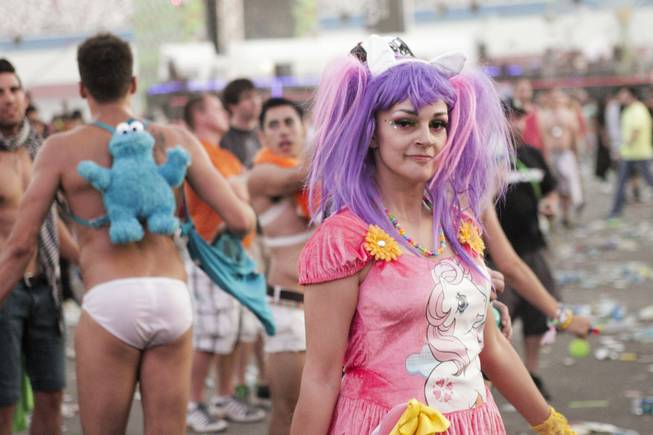 A man wearing a Cookie Monster backpack is seen in the background as a woman in a "My Little Pony"-themed outfit walks by during Headhunterz's set at the Electric Daisy Carnival at Las Vegas Motor Speedway on Sunday, June 23, 2013.