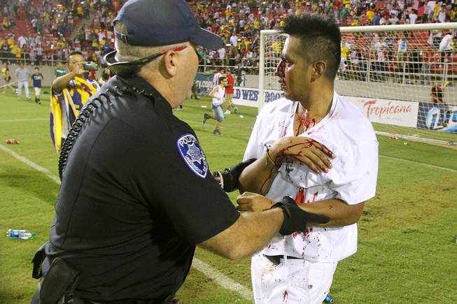 A bloodied soccer fan is led off the field by a UNLV policeman after El Super Clasico soccer game Wednesday, July 3, 2013 at Sam Boyd Stadium.