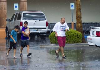 A family heads to their car after grocery shopping during a rainstorm in Henderson Sunday, July 7, 2013. (No names provided).