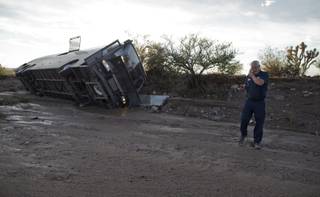 A tow truck driver talks on his cell phone after assessing the location of a tour bus which was caught in flash flood waters and pushed down a wash about 300 yards from the road, Sunday, July 28, 2013, near Dolan Springs, Ariz. 