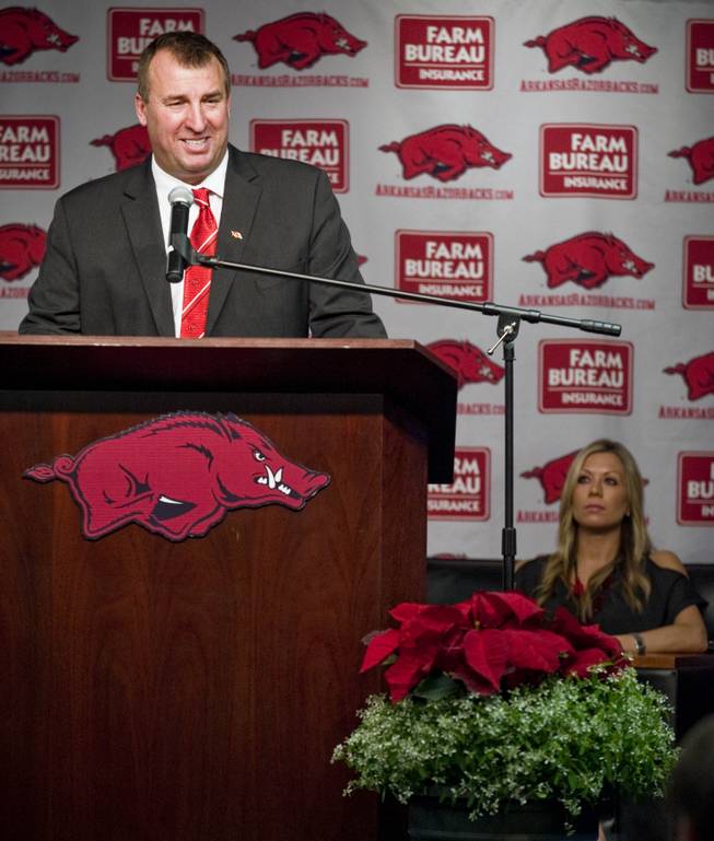 Arkansas football coach Bret Bielema, left, speaks to the media as his wife, Jen, rear right, looks on during a news conference to announce Bielema's hire in Fayetteville, Ark., Wednesday, Dec 5, 2012. Bielema, who left Wisconsin for Arkansas, will be paid $3.2 million annually for six years.