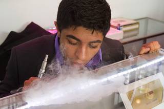 Ahmed Tebha, store manager of Evapor8, a hookah lounge and vapor boutique, performs a trick with water vapor from an e-cigarette after a ribbon-cutting ceremony at the Neonopolis Mall in downtown Las Vegas Thursday, Aug. 8, 2013.
