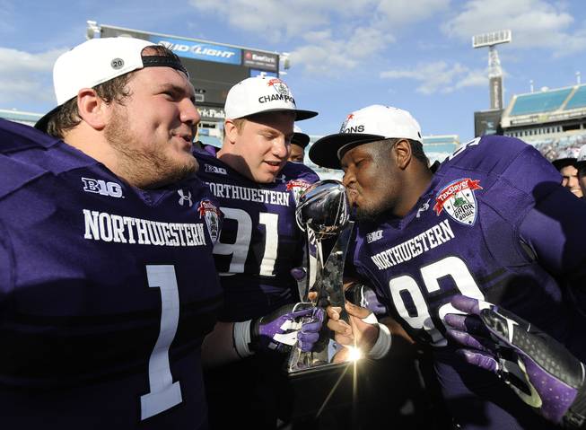 Northwestern defensive lineman Brian Arnfelt (91) and Bo Cisek (1) holds the trophy while their teammate Will Hampton (92) kisses it after the Gator Bowl NCAA college football game against Mississippi State, Tuesday, Jan. 1, 2013 in Jacksonville, Fla. Northwestern won 34-20.
