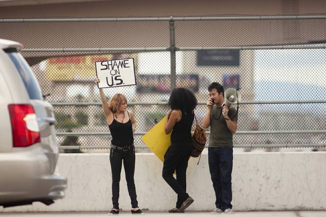 A woman holds up a "Sham on U.S." sign to oncoming traffic during a protest against U.S. intervention in Syria held on Tropicana and the I-15, Saturday, Aug. 31, 2013.
