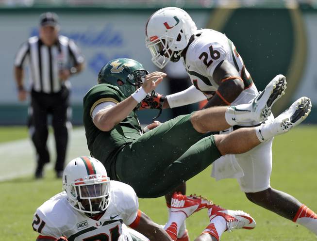 Miami defensive back Antonio Crawford (21) and defensive back Rayshawn Jenkins (26) team up to send South Florida quarterback Steven Bench flying on a third quarter tackle during an NCAA college football game Saturday, Sept. 28, 2013, in Tampa, Fla. Miami won the game 49-21.
