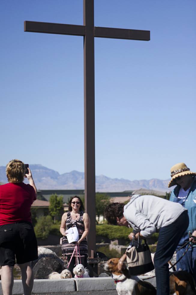 An attendee has her picture taken with her dogs in front of a giant cross during a pet blessing ceremony to celebrate the Feast of St. Francis of Assisi, the Catholic patron saint of animals, at New Song Church in Henderson on Saturday, Oct. 5, 2013.
