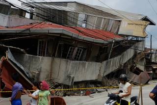 Residents walk past a damaged structure in Cebu, central Philippines on Tuesday Oct. 15, 2013. A 7.2-magnitude earthquake struck in the central Philippines on Tuesday morning, collapsing roofs and buildings, cracking walls and roads and killing several people.