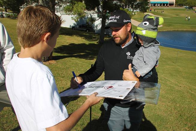 Holding his son Tucker, Ryan Moore signs an autograph during the Shriners Hospital for Children Open pro-am tournament Wednesday, Oct. 16, 2013.