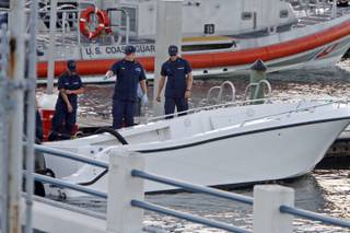 U.S Coast Guard personnel inspects a vessel with a missing center console that capsized near Miami,  Wednesday Oct. 16, 2013.  The Coast Guard responded to an early morning call and found nine people clinging to the hull seven miles east of Miami.  Four women died and 10 other people were taken into custody after the boat with more than a dozen people aboard, including Haitian and Jamaican nationals, capsized in the waters off South Florida.  Authorities are investigating whether the victims and survivors were part of a human smuggling operation.