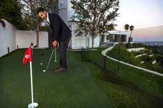 Real estate agent Mauricio Umansky putts with a Scotty Cameron putter, which is included in the sale of $36 million Beverly Hills home, Thursday, Oct. 17, 2013. The home is move-in ready. Amenities aren't always enough to sell a house anymore. Convenience has a place too as more homes are being offering fully furnished and stocked with items include linens, liquor and accessories.