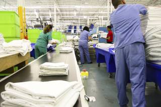 Freshly ironed and folded sheets travel along a conveyer belt as employees prepare them to be bundled for client delivery during a walk-through of Apex Linen in Las Vegas Tuesday, October 30, 2013.
