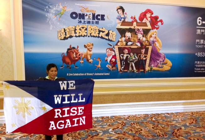 A woman holds up a "We Will Rise Again" flag in front of a giant ad advertising Disney on Ice at the Venetian Macau.