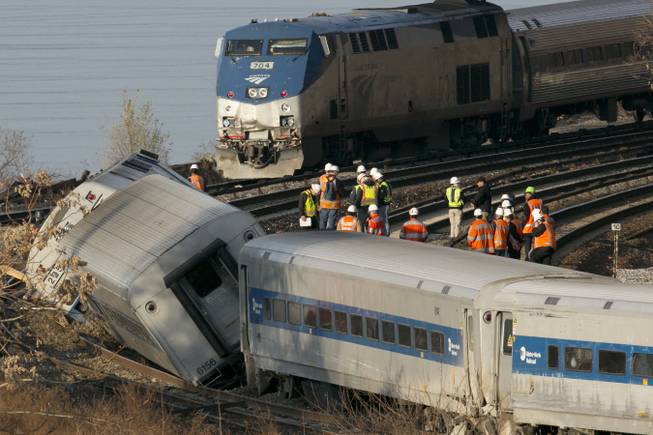 An Amtrak train, top, traveling on an unaffected track, passes a derailed Metro North commuter train, Sunday, Dec. 1, 2013 in the Bronx borough of New York. Officials are standing on a curve in the tracks where the Metro North train derailed.