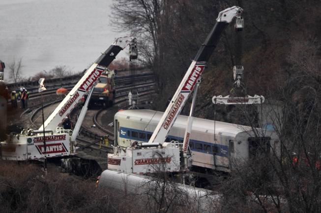 Cranes lift a derailed Metro-North train car, Monday, Dec. 2, 2013, in the Bronx borough of New York. Federal authorities began righting the cars Monday morning as they started an exhaustive investigation into what caused a New York City commuter train rounding a riverside curve to derail, killing four people and injuring more than 60 others. A second "event recorder" retrieved from the train may provide information on the speed of the train, how the brakes were applied, and the throttle setting, a member of the National Transportation Safety Board said Monday.