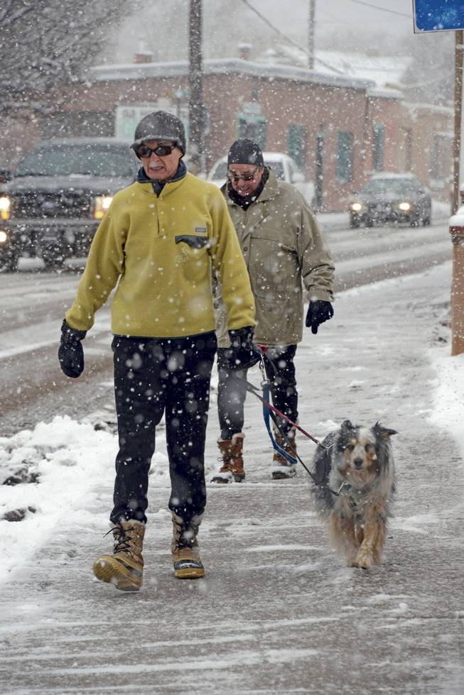 Melina and Gary Hall take a walk in the falling snow with their ten-year-old dog Roxie along the Old Santa Fe Trail in Santa Fe, N.M. Thursday, Dec. 5, 2013.  Some northern New Mexico highways have difficult driving conditions Thursday as the latest blast of freezing temperatures, wind and snow causes delays and closures in parts of the state. National Weather Service forecasters say snowfall accumulations in some areas could reach 6 to 8 inches, with hardest-hit areas expected to include Torrance County and north toward Las Vegas.