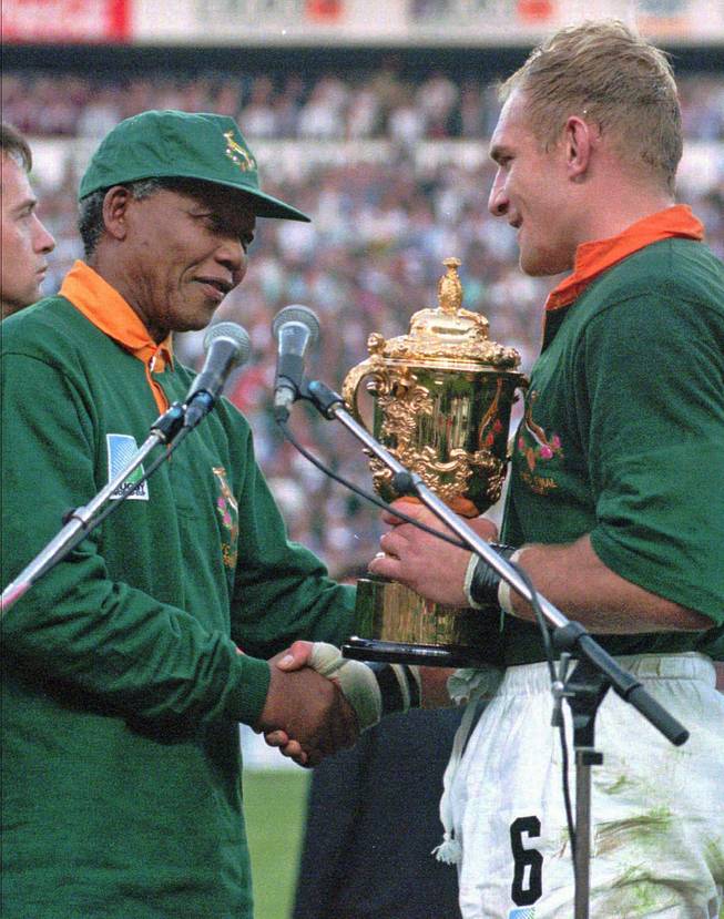 South African rugby captain Francios Pienaar, right, receives the Rugby World Cup from South African President Nelson Mandela, who wears a South African rugby shirt, after they defeated New Zealand in the final 15-12 at Ellis Park, Johannesburg, June 24, 1995.