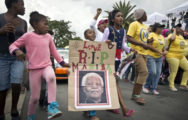 A young girl with a placard showing the face of Nelson Mandela and referring to his clan name "Madiba", marches with others to celebrate his life, in the street outside his old house in Soweto, Johannesburg, South Africa, Friday, Dec. 6, 2013. 