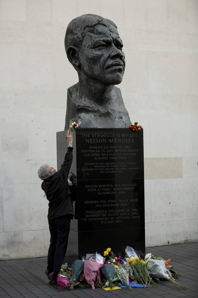 A woman lays flowers by the statue of former South African president Nelson Mandela, at the side of the Royal Festival Hall on the south bank of London, Friday, Dec. 6, 2013. 