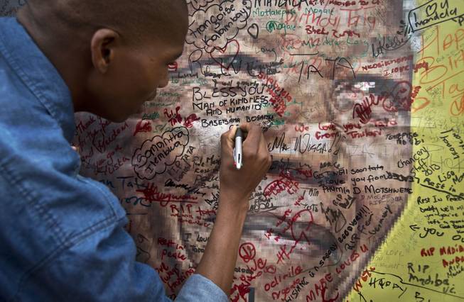A well-wisher writes a message on a poster of Nelson Mandela on which he and others have written their messages of condolence and support, in the street outside his old house in Soweto, Johannesburg, South Africa Friday, Dec. 6, 2013.
