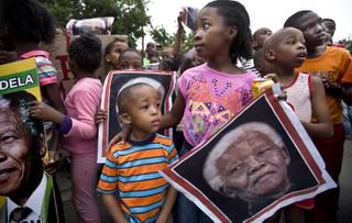 South African children hold placards showing the face of Nelson Mandela as they celebrate his life, in the street outside his old house in Soweto, Johannesburg, South Africa, Friday, Dec. 6, 2013. 