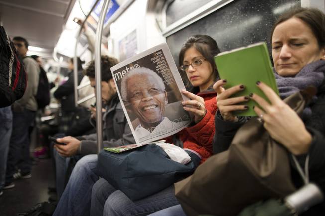 A subway rider reads a newspaper featuring news of the death of South African leader Nelson Mandela, Friday, Dec. 6, 2013, in New York. South Africa's first black president died Thursday after a long illness. He was 95.