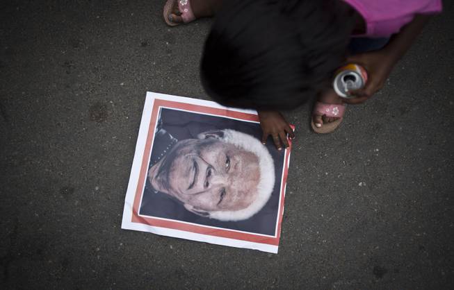 A girl picks up a poster showing the face of Nelson Mandela after it fell to the ground, as she and others celebrate his life, in the street outside his old house in Soweto, Johannesburg, South Africa Friday, Dec. 6, 2013. 
