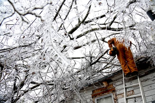 Randy Dean carries a chain saw down from his roof in Paris, Texas, on Saturday, Dec. 7, 2013. Electrical crews are coming into northeast Texas to help restore power to thousands of residents after an ice storm caused trees and branches to snap, pulling down lines and blowing up transformers.