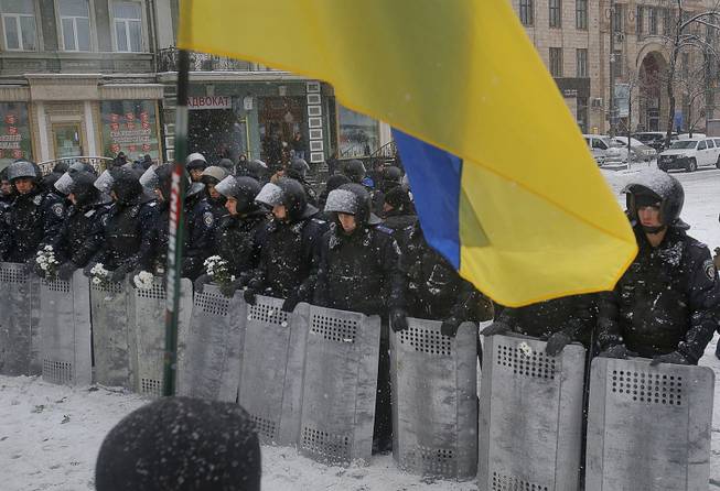 A Ukrainian national flag is waved by pro-European protesters as Ukrainian riot police block the road next to Pro-European Union activists gathered on the Independence Square in Kiev, Ukraine, Monday, Dec. 9, 2013.
