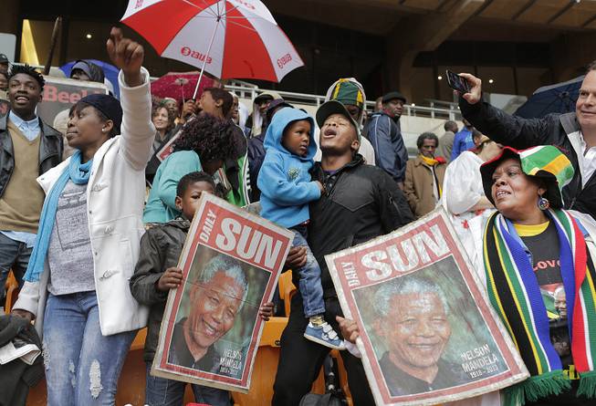 People hold images of former South African president Nelson Mandela ahead of his memorial service at the FNB Stadium in Soweto, near Johannesburg, South Africa, Tuesday Dec. 10, 2013. 