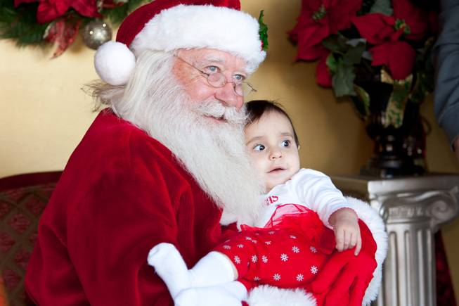 Visiting Santa for the first time, ten-month-old Annalisa Hamill smiles while having her picture taken in his cottage at Tivoli Village in Las Vegas Friday, December 13, 2013.  Larry Hansen has been donning the coveted suit and sharing the spirit of Santa for over nine years in Las Vegas.